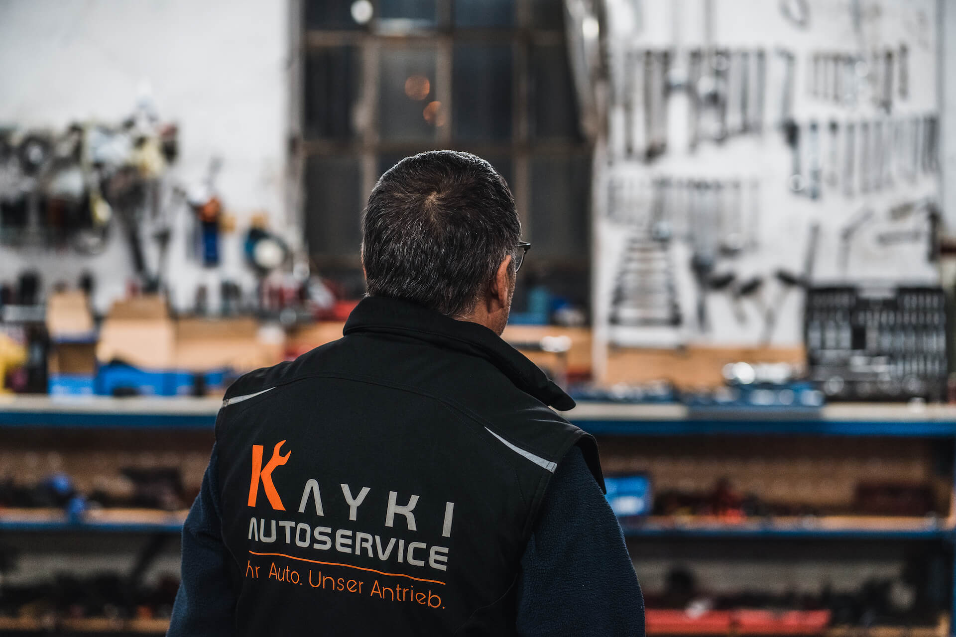 Mechaniker in einer Werkstatt in Hildesheim mit Blick auf Werkzeugwand, erkennbar am Logo von Kayki-Autoservice auf seiner Arbeitskleidung.