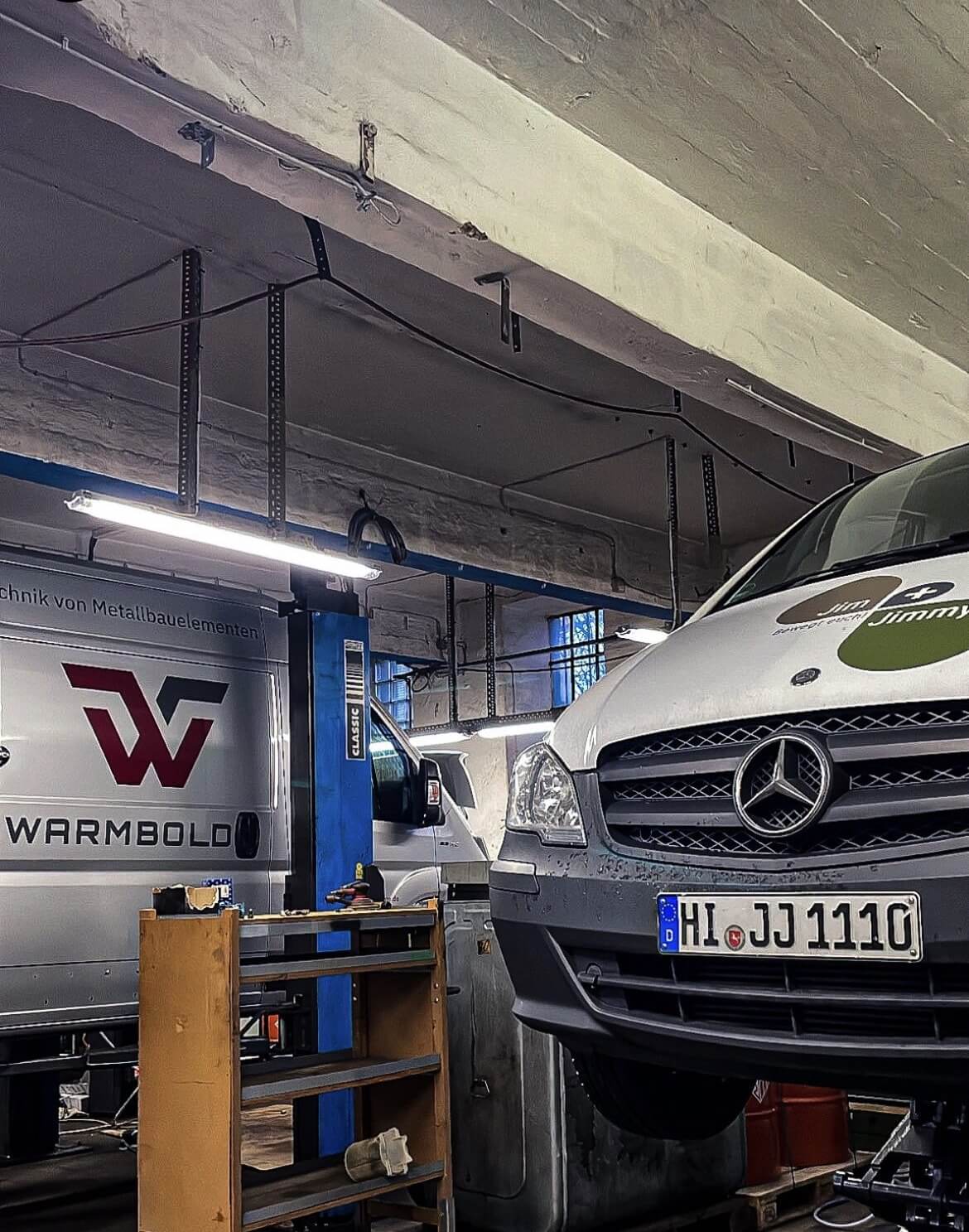 Weißer Mercedes Transporter auf einer Hebebühne in einer Werkstatt mit Service für Firmenflotten, erkennbar an den Logos und Werbung für technische Dienstleistungen